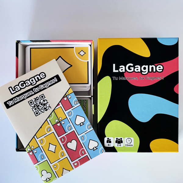 Photo de la boîte du jeu "LaGagne" et de la règle du jeu, montrant le design coloré de la boîte et les instructions de jeu à côté.